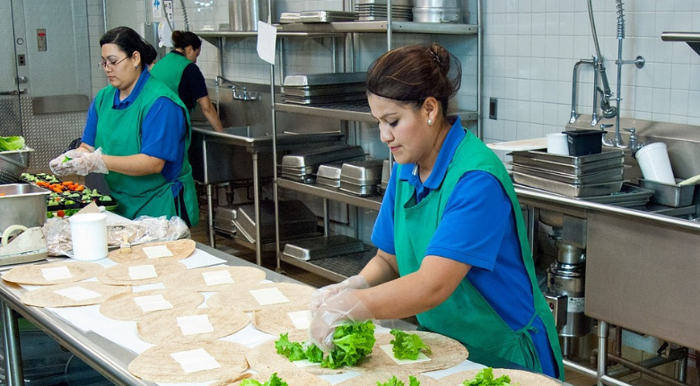 two women assembling wraps in a commercial kitchen