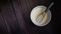 whisk in a bowl of pancake batter on a dark wooden table whisk in a bowl of pancake batter on a dark wooden table