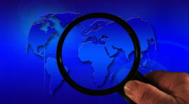 world map with han holding magnifying glass over it
