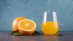 glass of orange juice next to orange halves