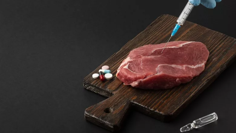 meat on cutting board next to pills with gloved hand injecting syringe into meat