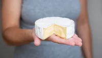 person holding wheel of soft cheese