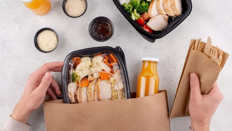 person pulling packaged food out of paper bag and holding disposable cutlery