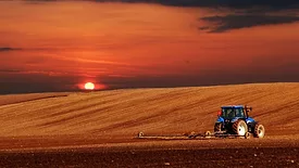 sun rising over a tractor plowing a farm field