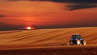 sun rising over a tractor plowing a farm field
