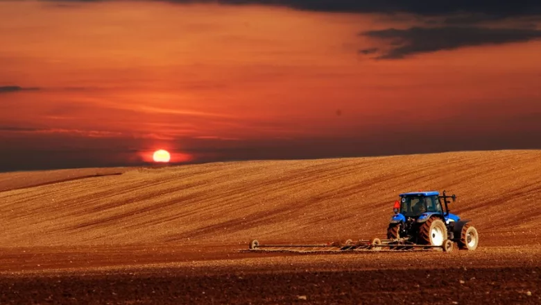 sun rising over a tractor plowing a farm field