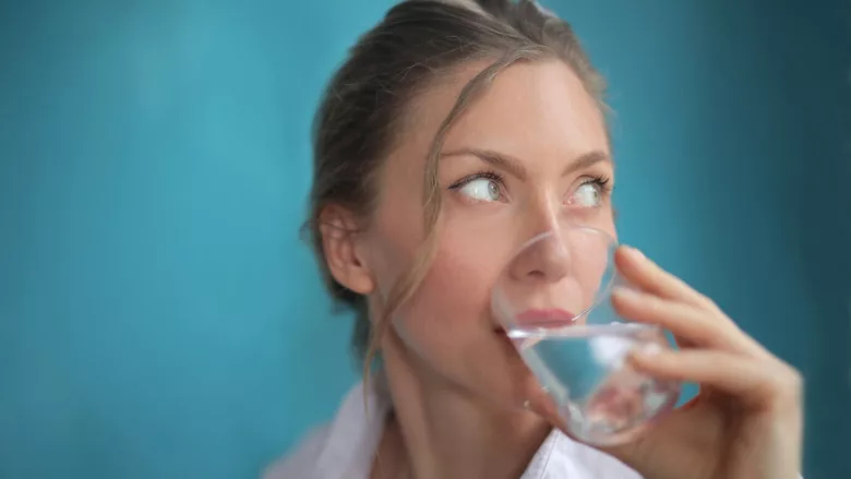 woman drinking water from a glass blue background