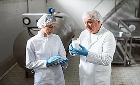 quality assurance professionals in milk production facility holding tablets and examining a glass of milk 