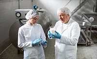 quality assurance professionals in milk production facility holding tablets and examining a glass of milk 