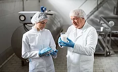 quality assurance professionals in milk production facility holding tablets and examining a glass of milk 