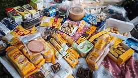 a spread of ultra-processed snacks, meats, and sweets on a picnic blanket outside