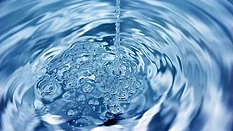 a stream of water falling into a swirling pool of clear blue