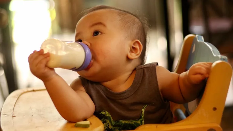 cute baby in high chair feeding himself a bottle