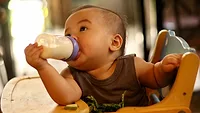 baby in high chair self-feeding bottle_HÂN NGUYỄN via Pexels.png cute baby in high chair feeding himself a bottle