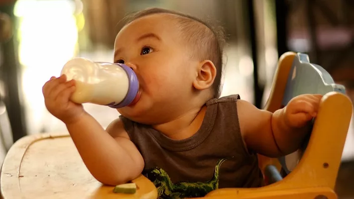 cute baby in high chair feeding himself a bottle