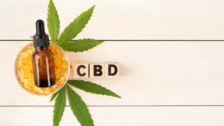 cbd oil, hemp leaves, and letters spelling CBD on wooden backdrop