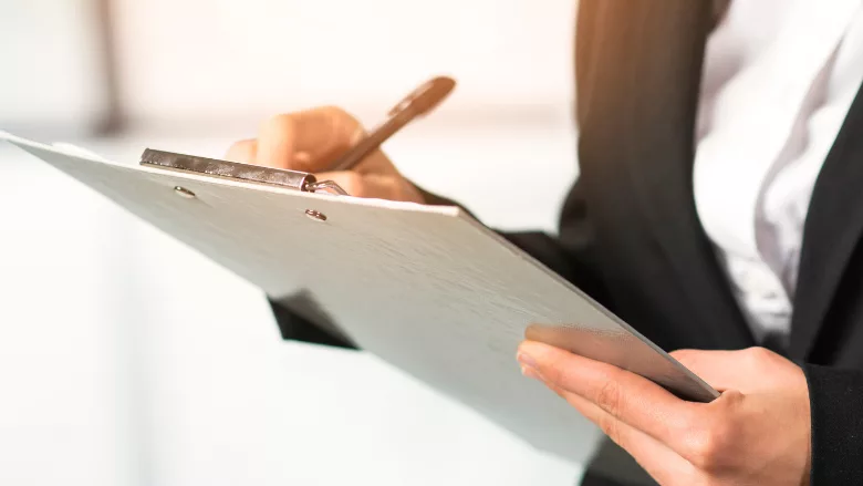 close-up of woman in suit writing on clipboard