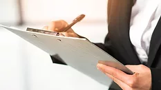 close-up of woman in suit writing on clipboard