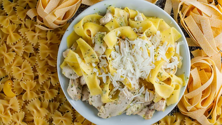 dried pastas surrounding a plate of prepared cheesy chicken pasta