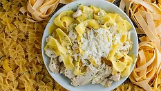 dried pastas surrounding a plate of prepared cheesy chicken pasta