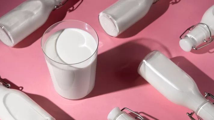 glass of milk and glass bottles of milk arranged against a pink background still life