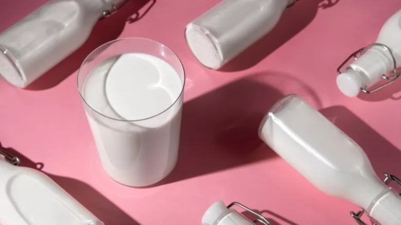 glass of milk and glass bottles of milk arranged against a pink background still life