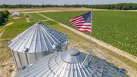 grain silos with US flag on top overlooking field of crops