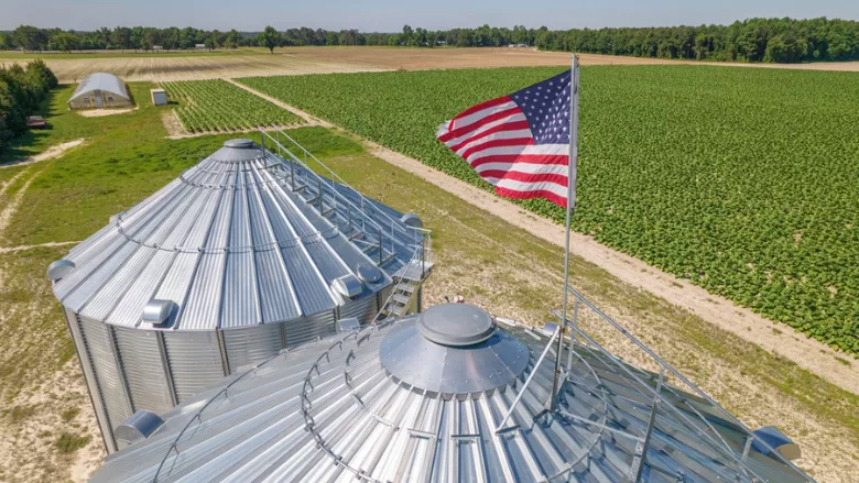 grain silos with US flag on top overlooking field of crops