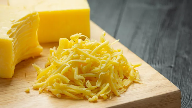 half shredded block of cheddar cheese and pile of cheese shreds on wooden cutting board