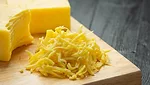 half shredded block of cheddar cheese and pile of cheese shreds on wooden cutting board