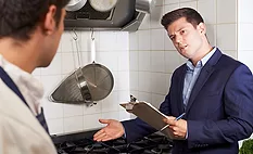 health inspector with clipboard talking to restaurant kitchen staff