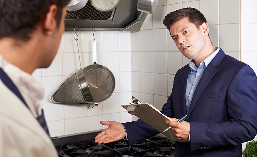 health inspector with clipboard talking to restaurant kitchen staff