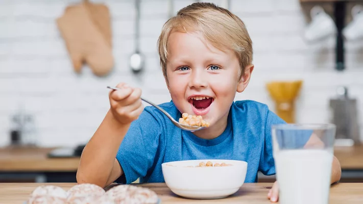 kid eating cereal with cookies and milk