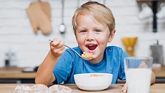 kid eating cereal with cookies and milk