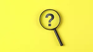 magnifying glass hovering over question mark on yellow background
