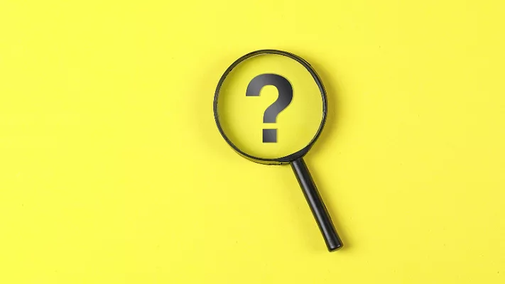 magnifying glass hovering over question mark on yellow background