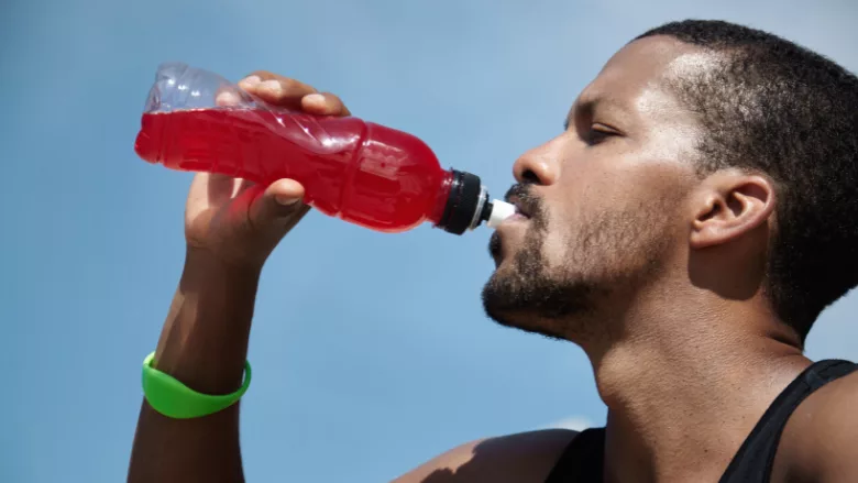 a man drinking a red sports drink from a bottle outside on a hot day