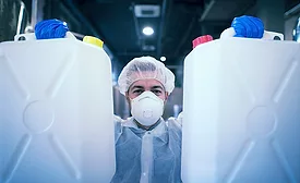 man in PPE holding two jugs of commercial disinfectant