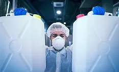 man in PPE holding two jugs of commercial disinfectant