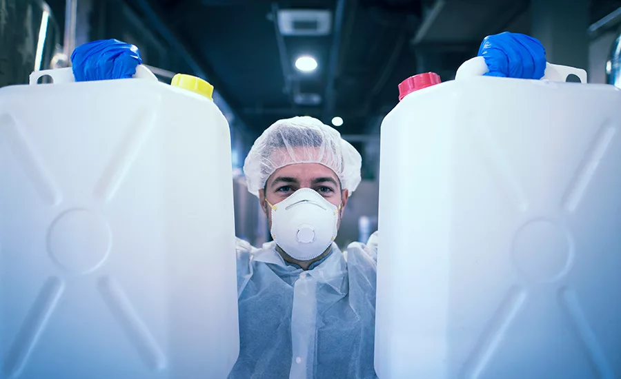 man in PPE holding two jugs of commercial disinfectant