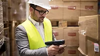 man in a suit with hard hat and reflective vest scanning barcode on box in warehouse