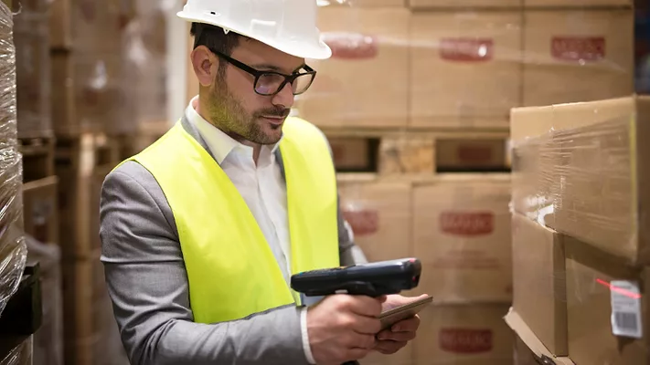 man in a suit with hard hat and reflective vest scanning barcode on box in warehouse