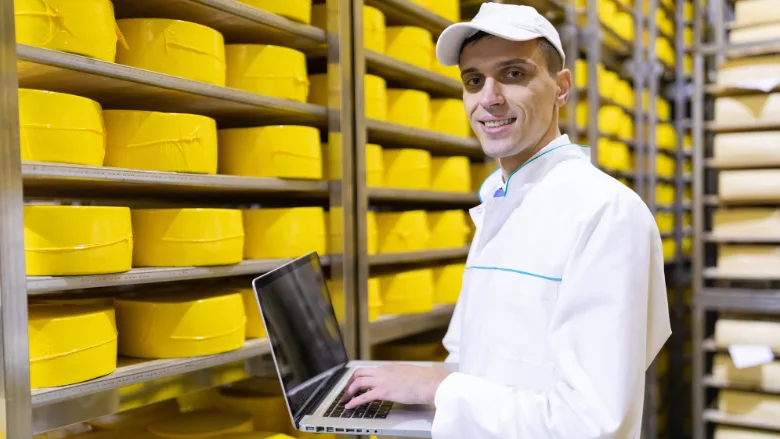 man working in a cheese warehouse smiling at camera holding laptop