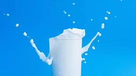 milk splashing out of a glass against a blue background