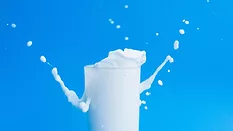 milk splashing out of a glass against a blue background
