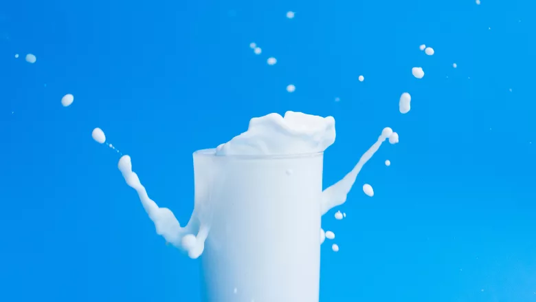 milk splashing out of a glass against a blue background
