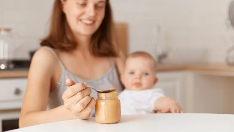 jar of baby food on table in foreground with mom holding baby in background