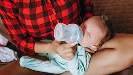 newborn baby in mom's lap taking a bottle