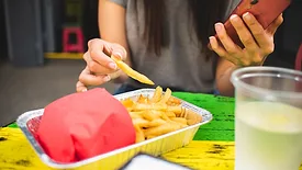 person holding phone while eating fries at foodservice establishment