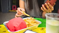 person holding phone while eating fries at foodservice establishment